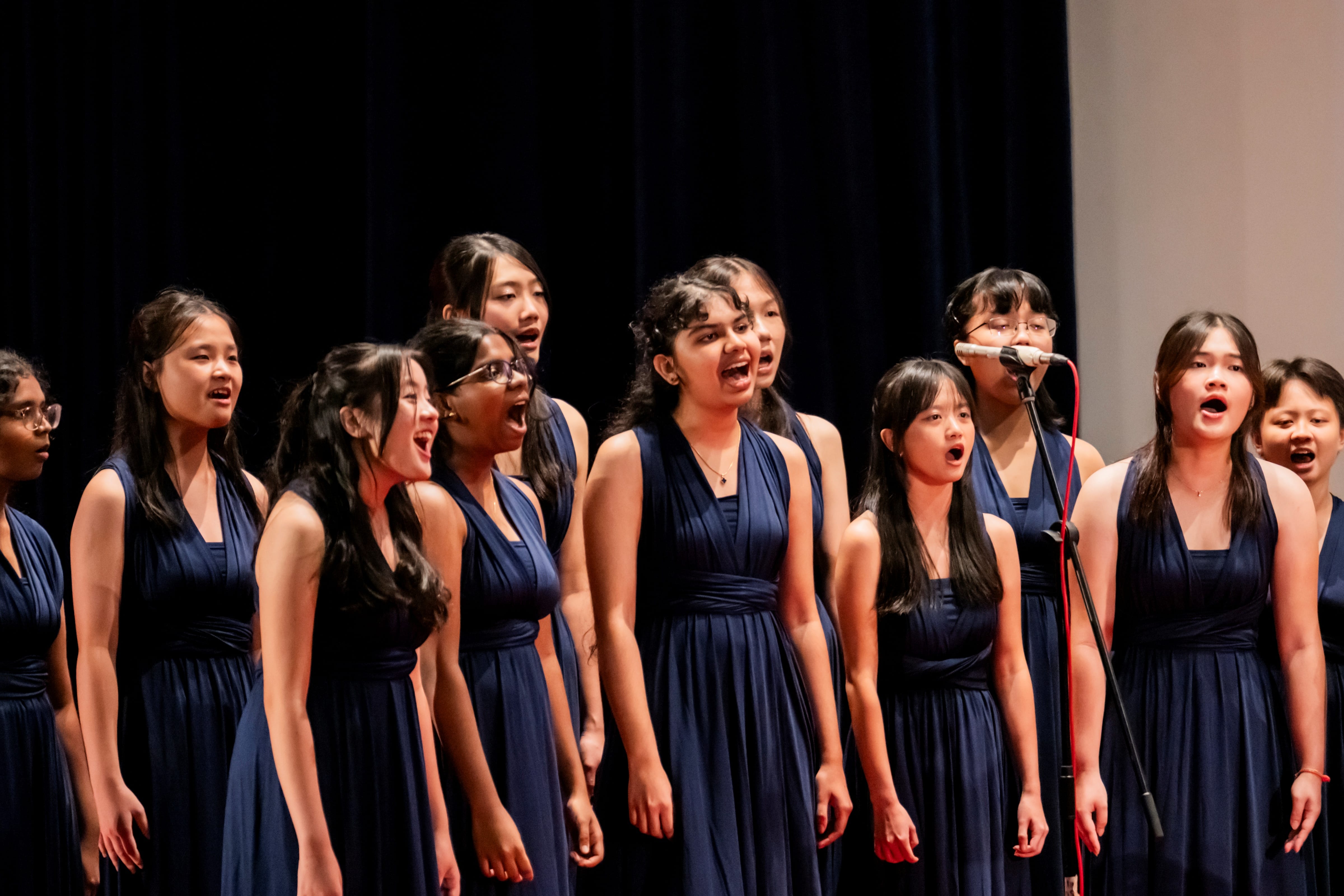 Female choir members in matching navy-blue dresses singing passionately during a stage performance.